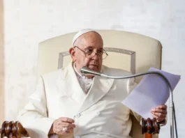 Pope Francis in a white suit holding a microphone and paper
